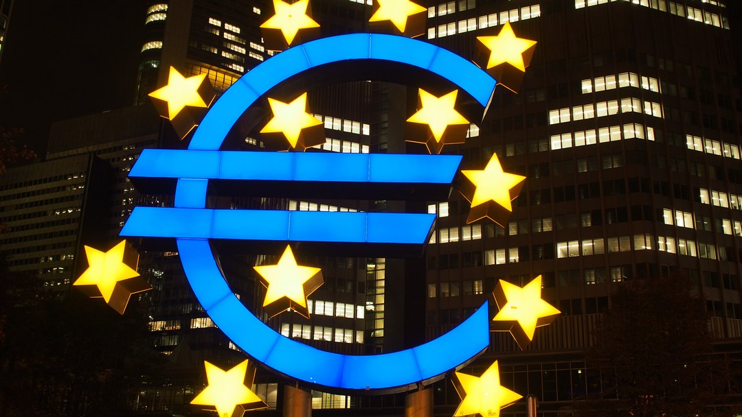 Signe euro lumineux devant un immeuble, la nuit.