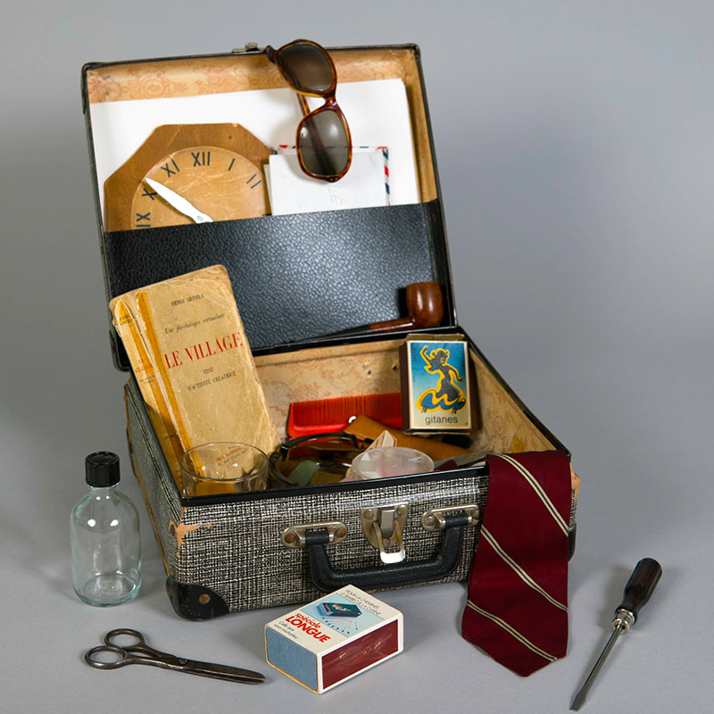 Vieille valise contenant une multitude d'objets : livre, boites d'allumettes, tournevis, ciseaux,....