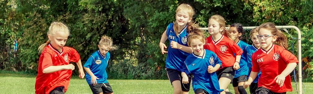 Match de football opposant deux équipes de filles d'une dizaine d'années, une en bleue, une en rouge.