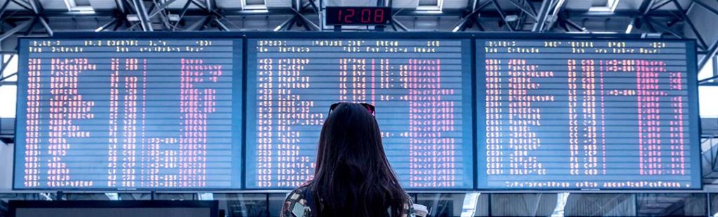 Jeune femme de dos consultant le panneau d'affichage des départs et arrivés dans un hall d'aéroport