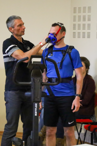 Un homme installe un maque à oxygène sur le visage d’un autre homme, en tenue de sport.